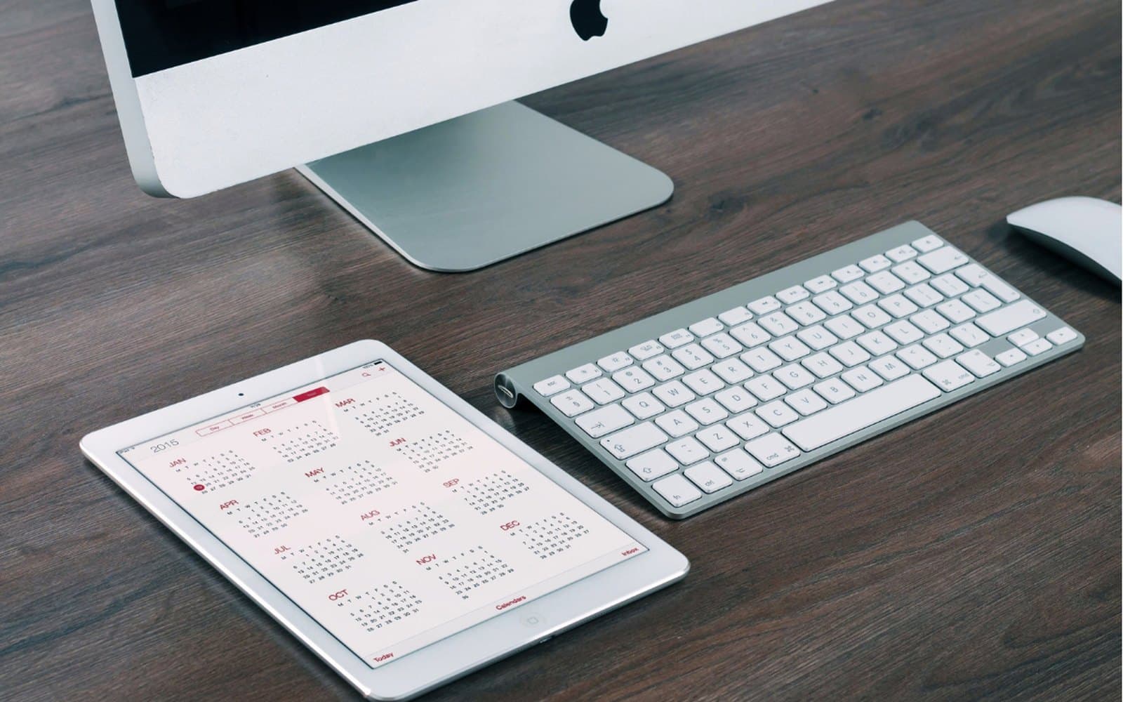 A calendar open on a tablet beside a keyboard on a wooden desk