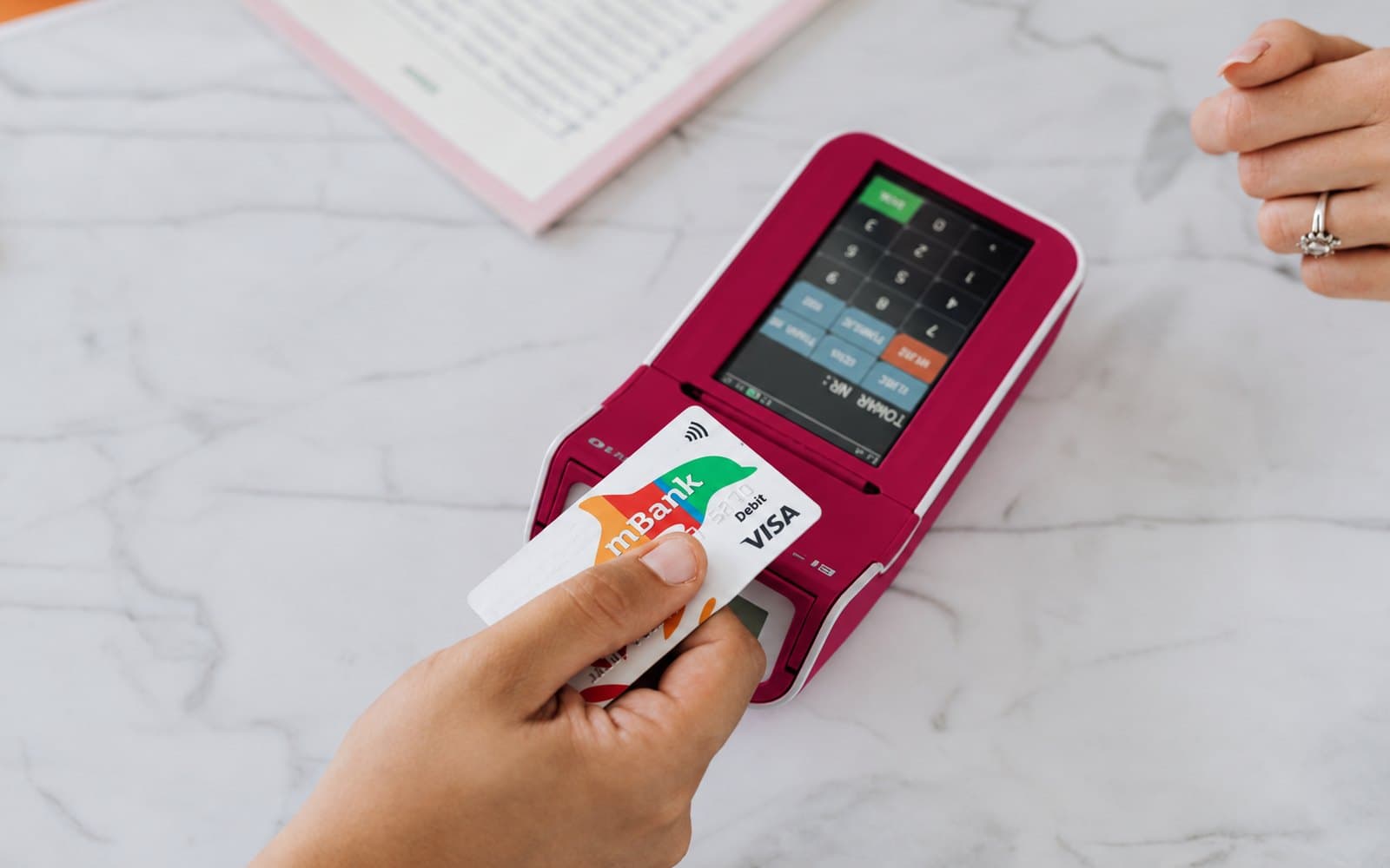 A hand tapping a card on a pink contactless payment terminal